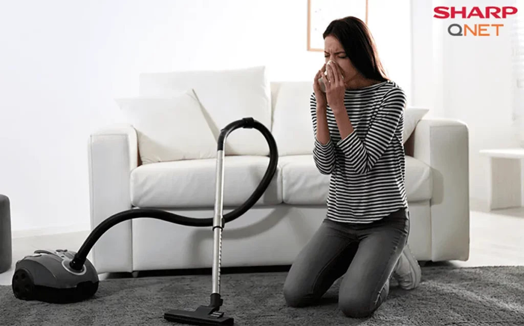 A young woman sneezing due to dust allergy symptoms while vacuuming the carpet in her home