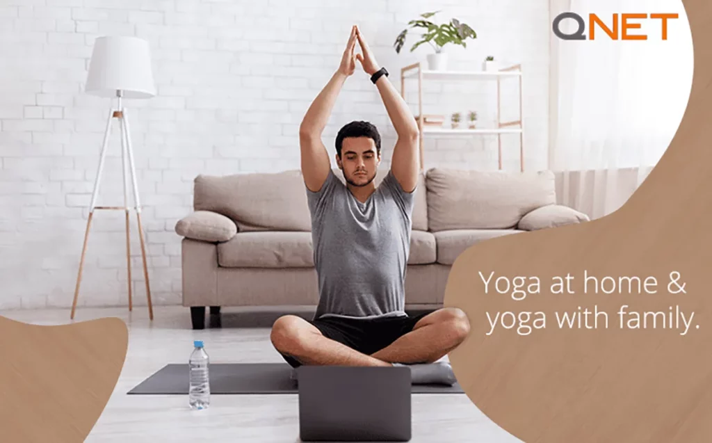 Young Indian man meditating in his house on the floor with a laptop in front of him.